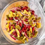 Three bean salad with kidney beans, green beans, yellow wax beans, and sliced red onion in a glass bowl.