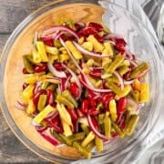 Three bean salad with kidney beans, green beans, yellow wax beans, and sliced red onion in a glass bowl.