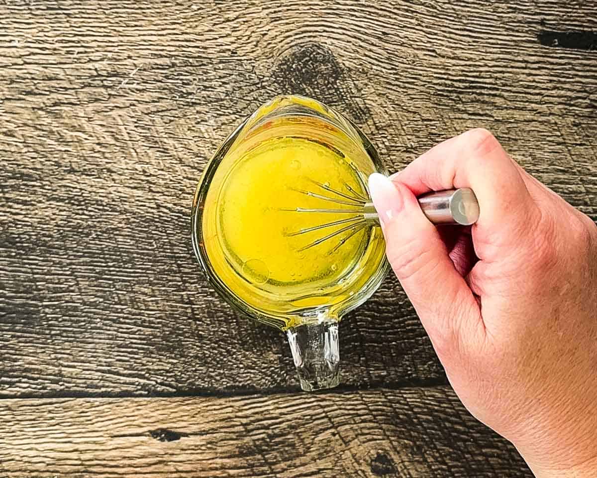 Whisking the dressing ingredients in a small measuring cup.