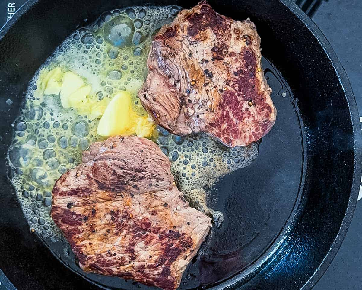 The butter and garlic added to the skillet with the seared steaks for the basting step.