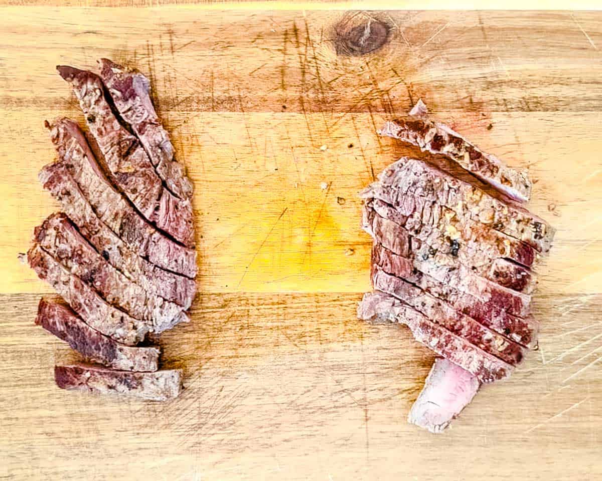 The steaks sliced thinly on a wooden cutting board.