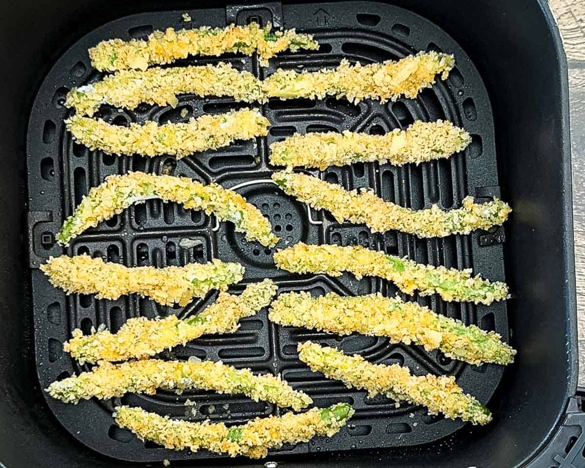 The breaded green beans in the air fryer basket.