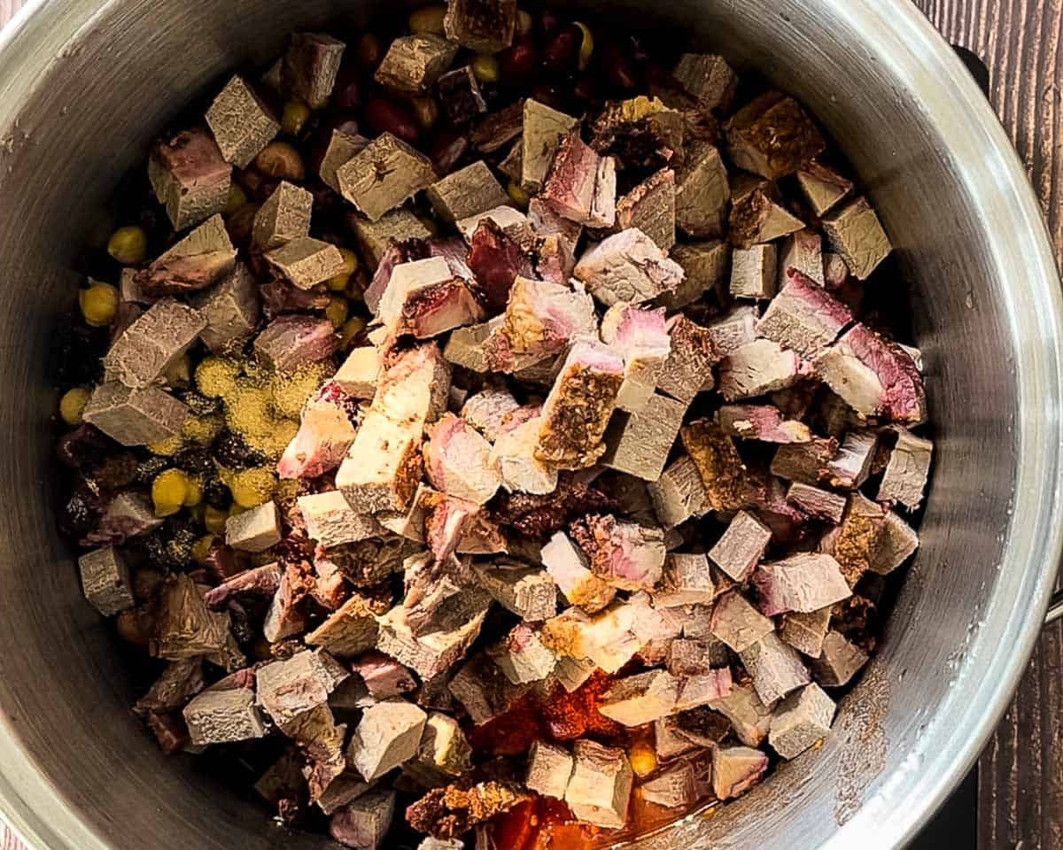 Cubed smoked brisket added to a pot with beans, tomatoes, and spices.