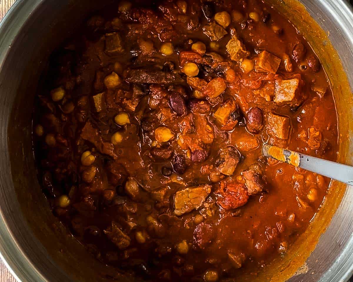 Thick smoked brisket chili in a pot with mixed beans, tomatoes, and chunks of smoked beef brisket.