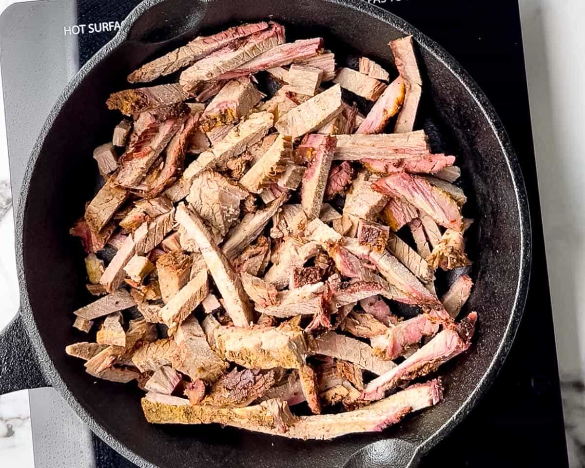 Leftover smoked brisket slices warming in a cast iron skillet on the stovetop.