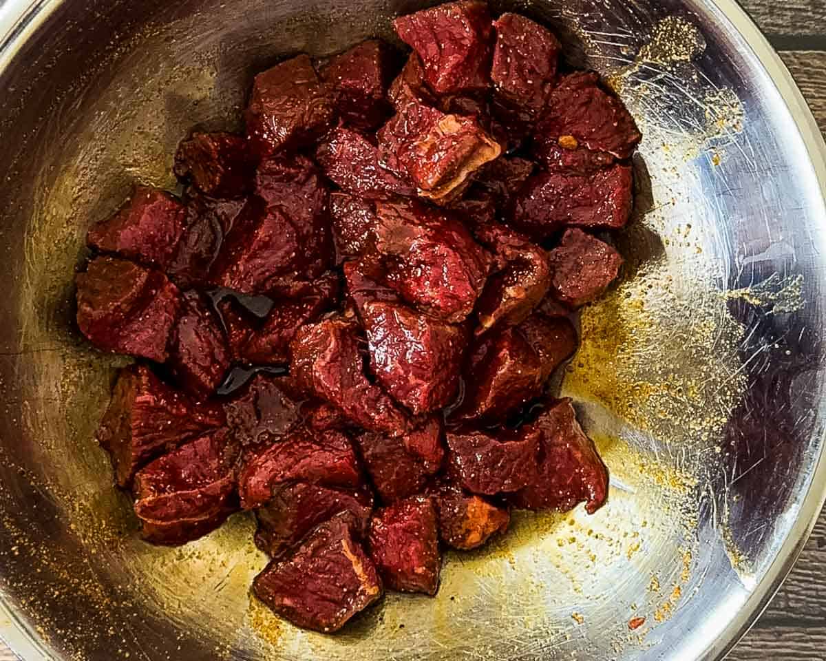 Steak cubes coated in a savory marinade in a metal bowl.