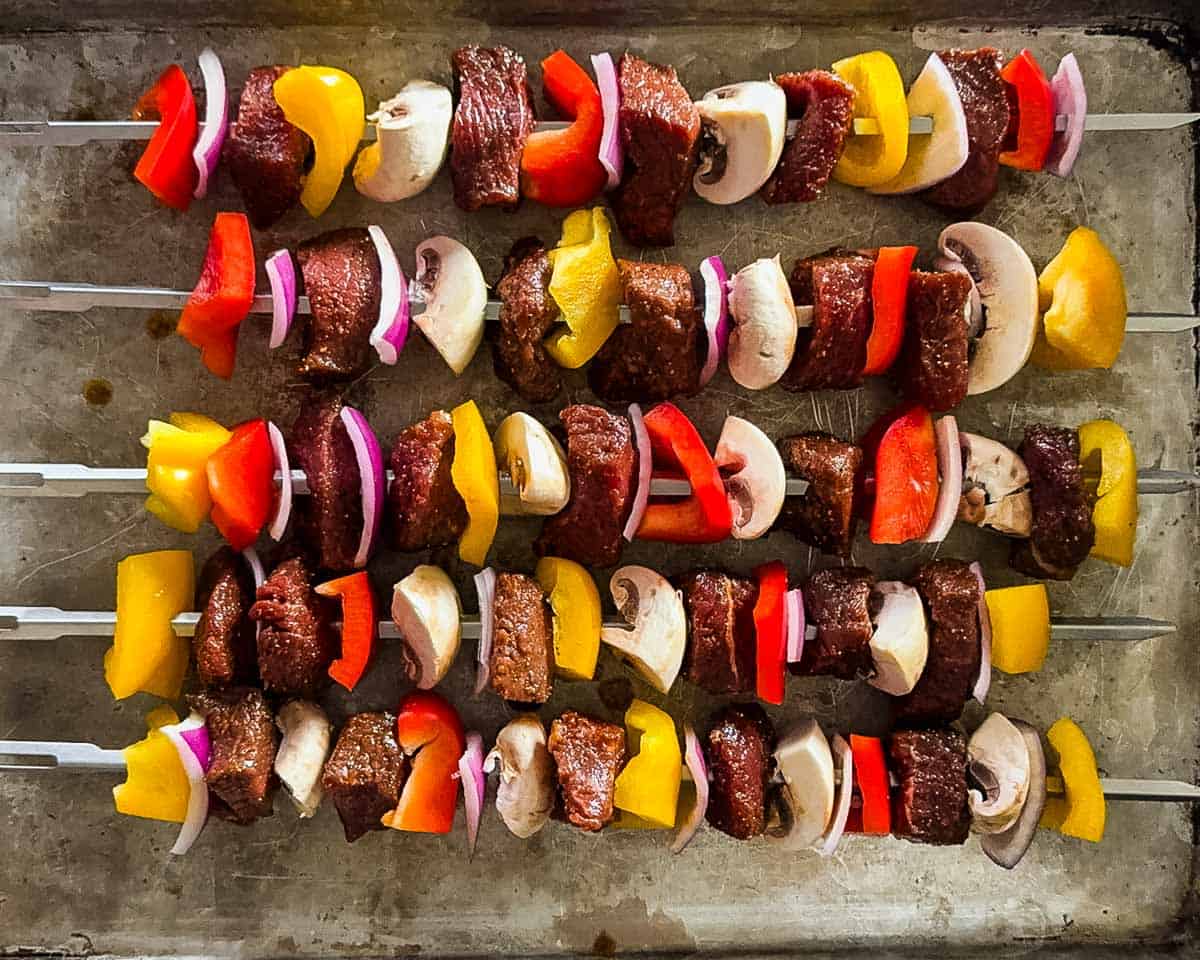Steak kabobs assembled with peppers, mushrooms, and onions spaced evenly on skewers.