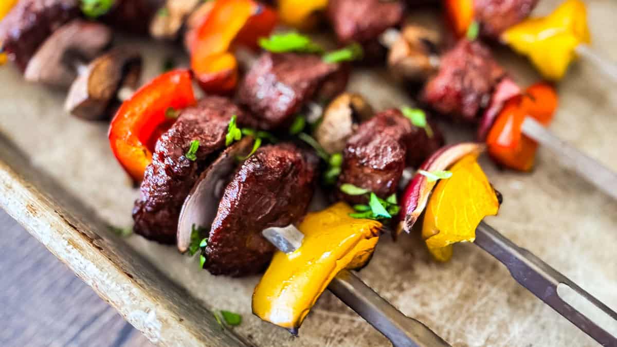 Smoked steak kabobs with top sirloin, mushrooms, bell peppers, and red onion on metal skewers.