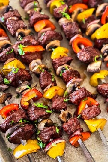 Smoked steak kabobs with top sirloin, mushrooms, bell peppers, and red onion on metal skewers.