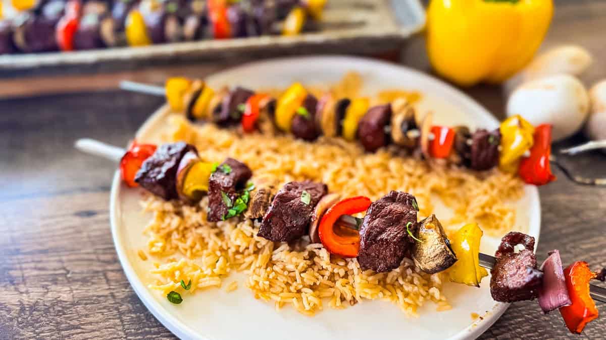 Smoked steak kabobs with peppers, mushrooms, and onions on a bed of rice on a dinner plate.