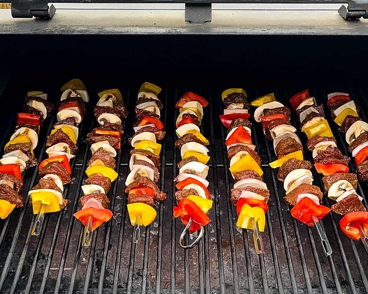 Kabobs cooking on grill grates during the smoking stage.