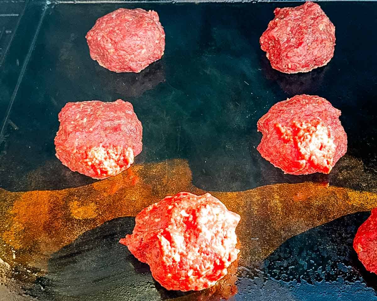 Balls of seasoned venison placed on a hot flat-top griddle before being smashed into burgers.