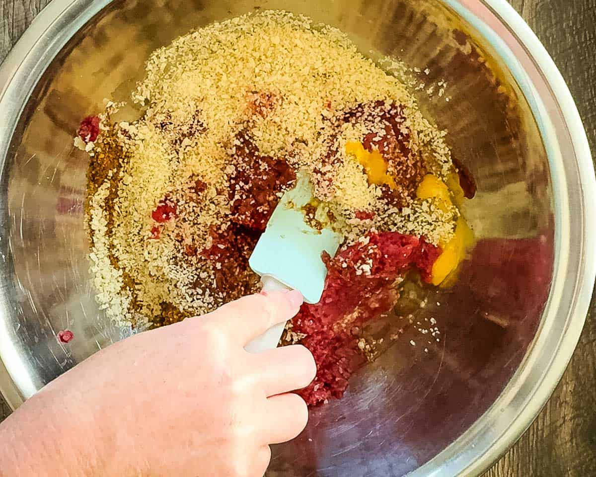 Mixing ground venison with panko, BBQ sauce, eggs, and seasonings in a large bowl for homemade venison smash burgers.