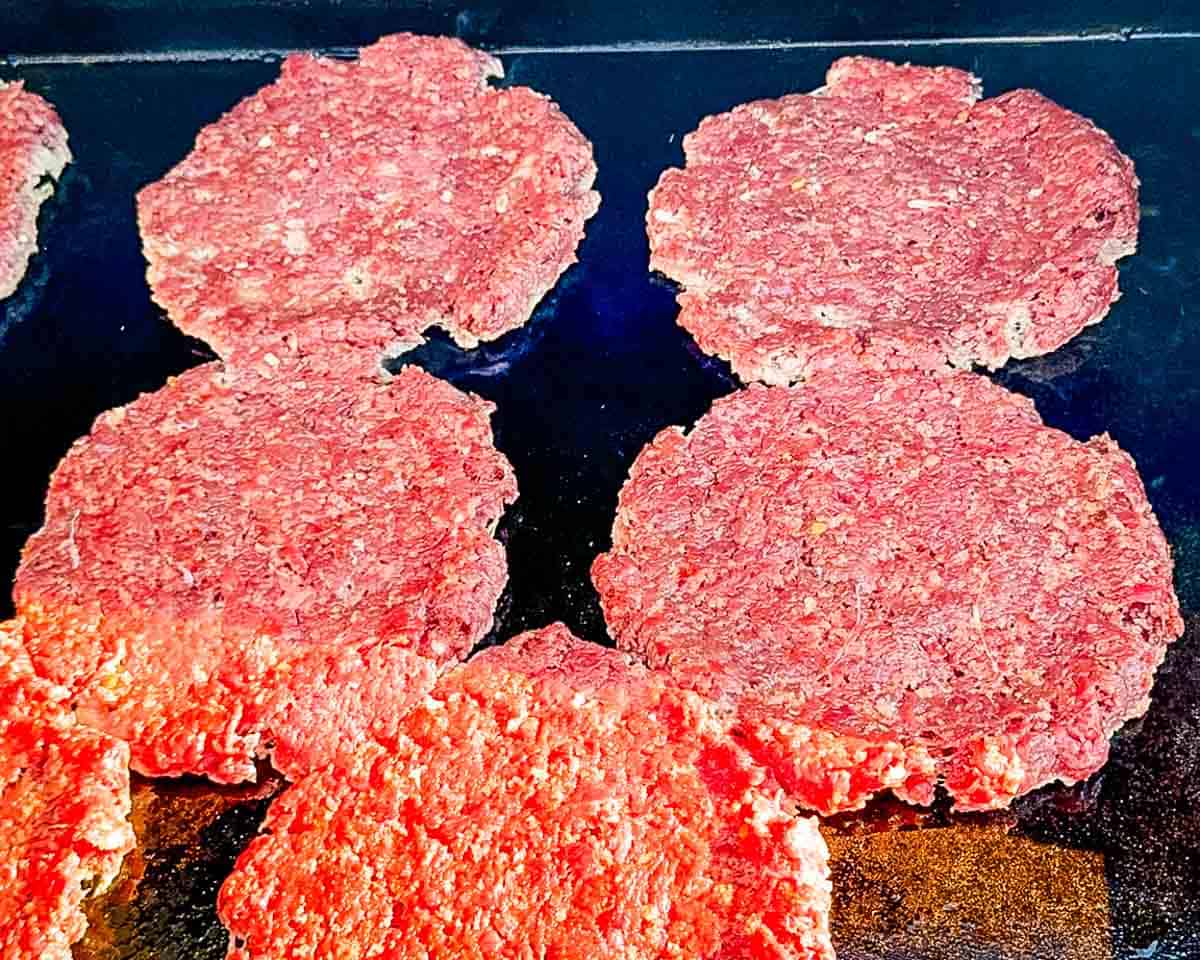 Venison smash burger patties flattened on a hot griddle and beginning to cook.