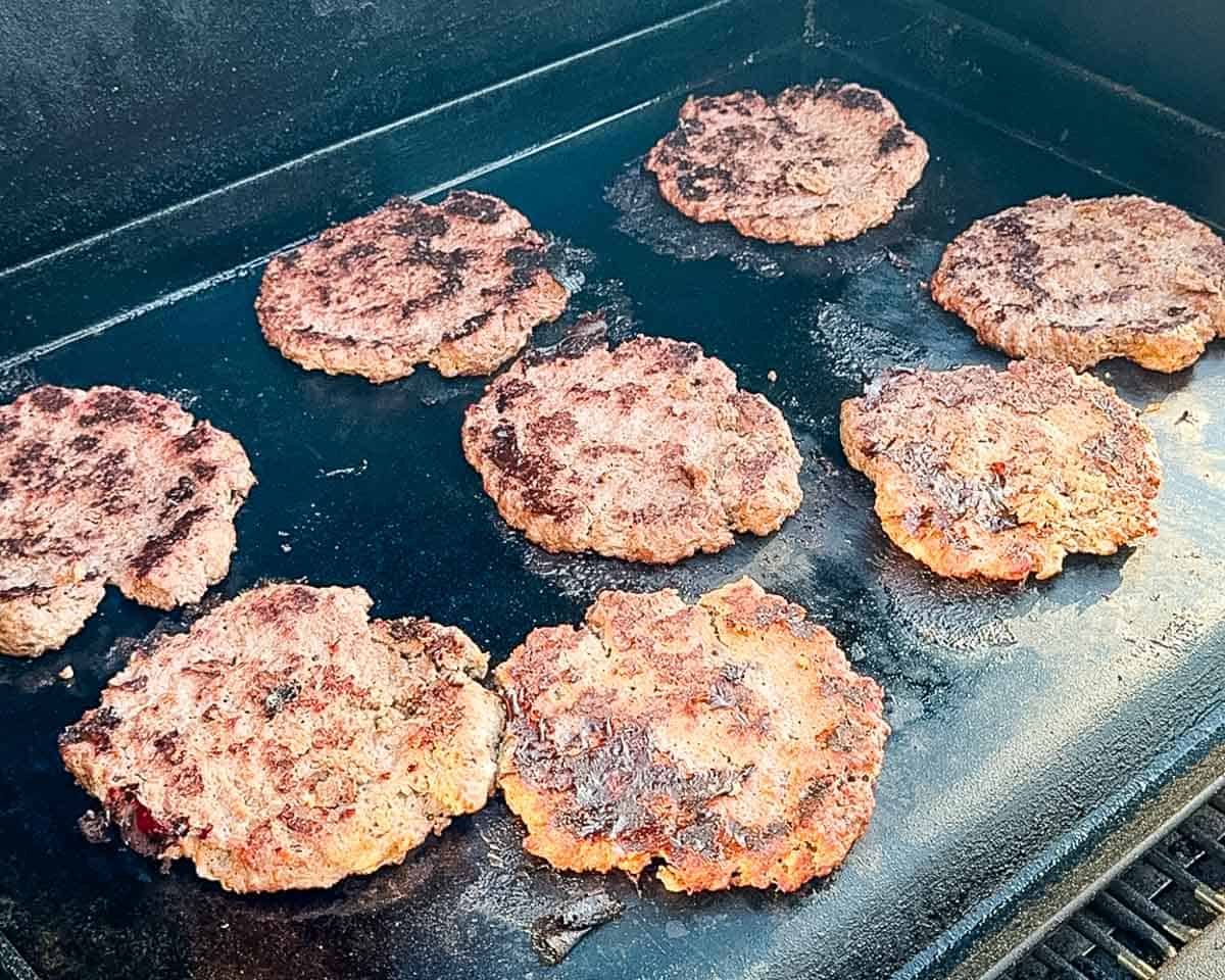 Venison smash burgers cooking on a flat-top griddle with crispy browned crusts after flipping.