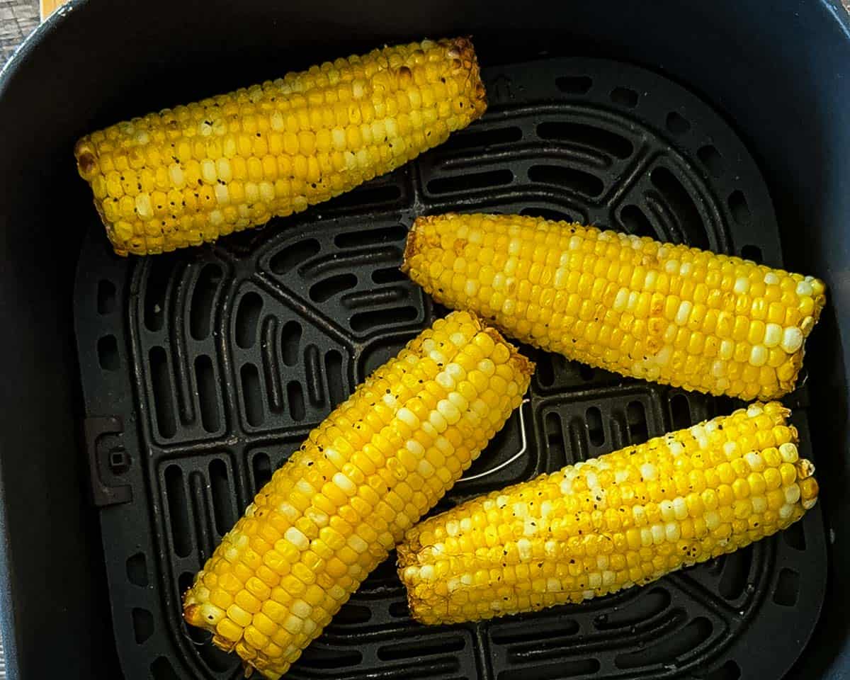 Cooked corn on the cob in the air fryer basket after cooking until tender and lightly browned.
