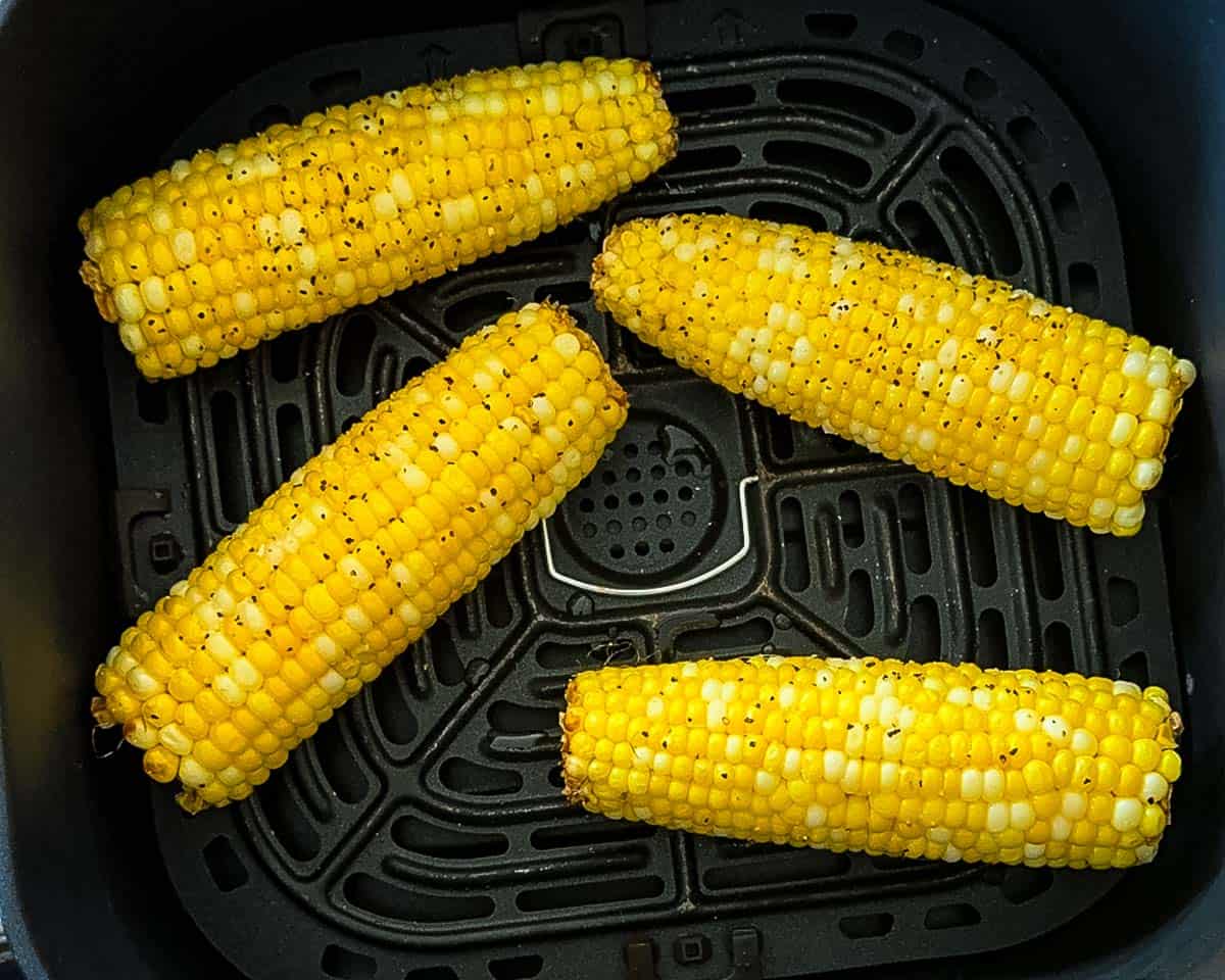 Corn on the cob in an air fryer basket halfway through cooking with light browning on the kernels.
