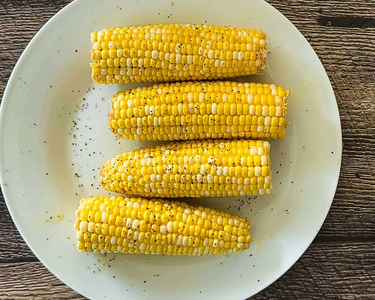 Corn on the cob seasoned with black pepper on a white plate before going into the air fryer.