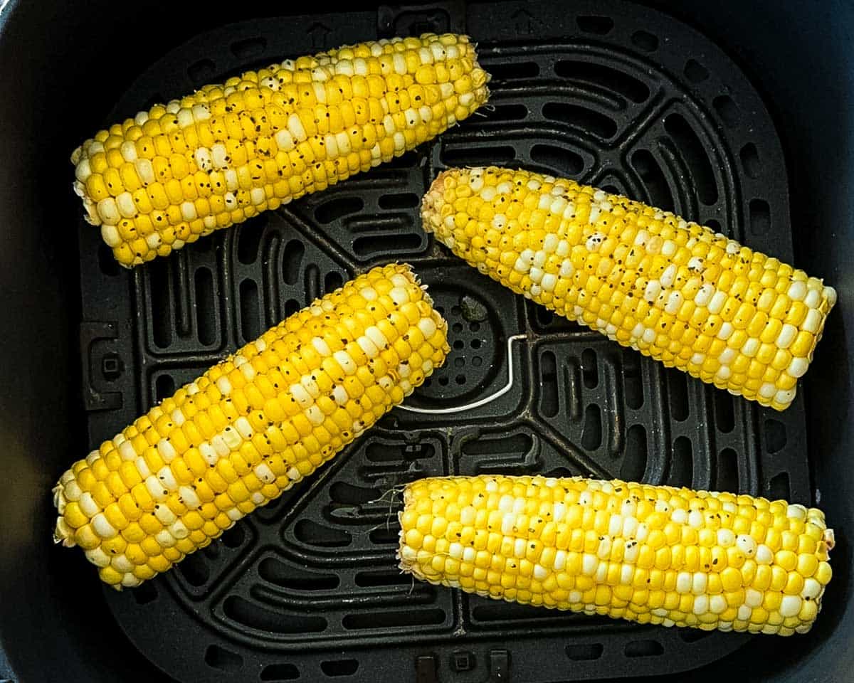 Seasoned corn on the cob arranged in a single layer in an air fryer basket before cooking.