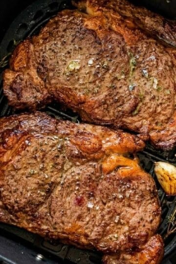 Finished air fryer steaks with a browned crust resting in the air fryer basket.