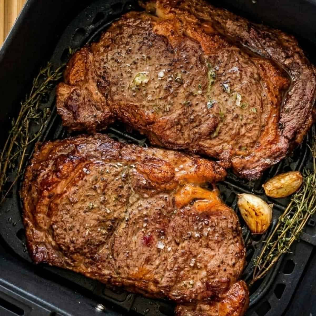 Finished air fryer steaks with a browned crust resting in the air fryer basket.