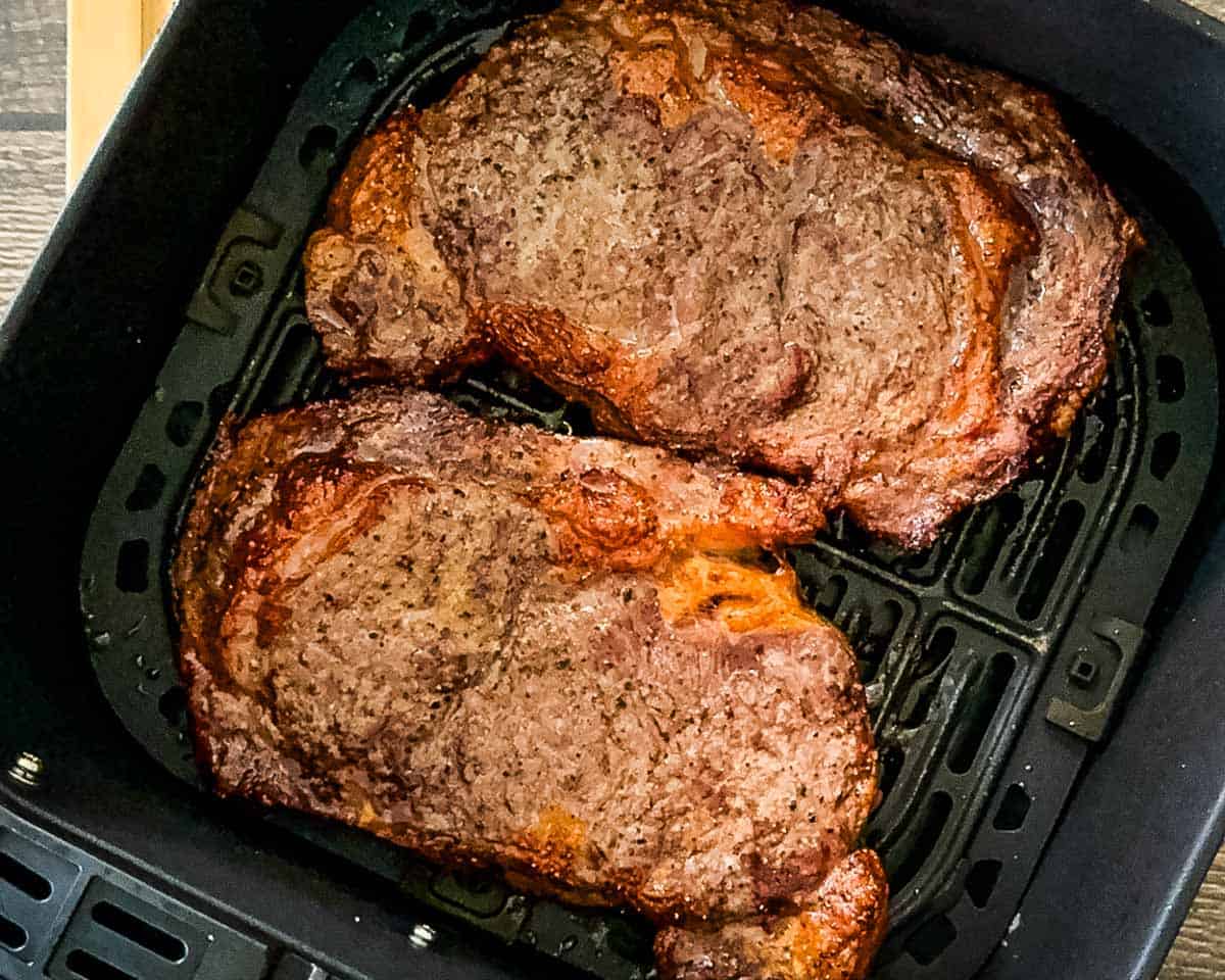Finished air fryer steaks with a browned crust resting in the air fryer basket.