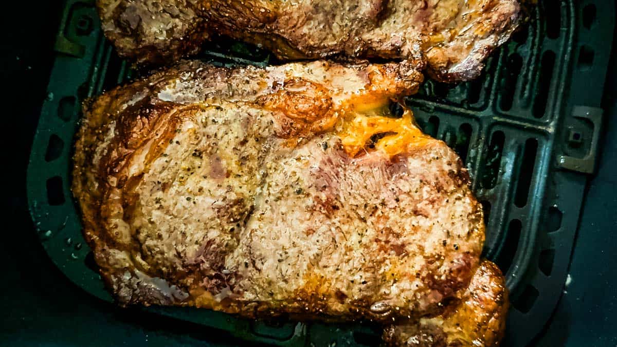 Finished air fryer steaks with a browned crust resting in the air fryer basket.