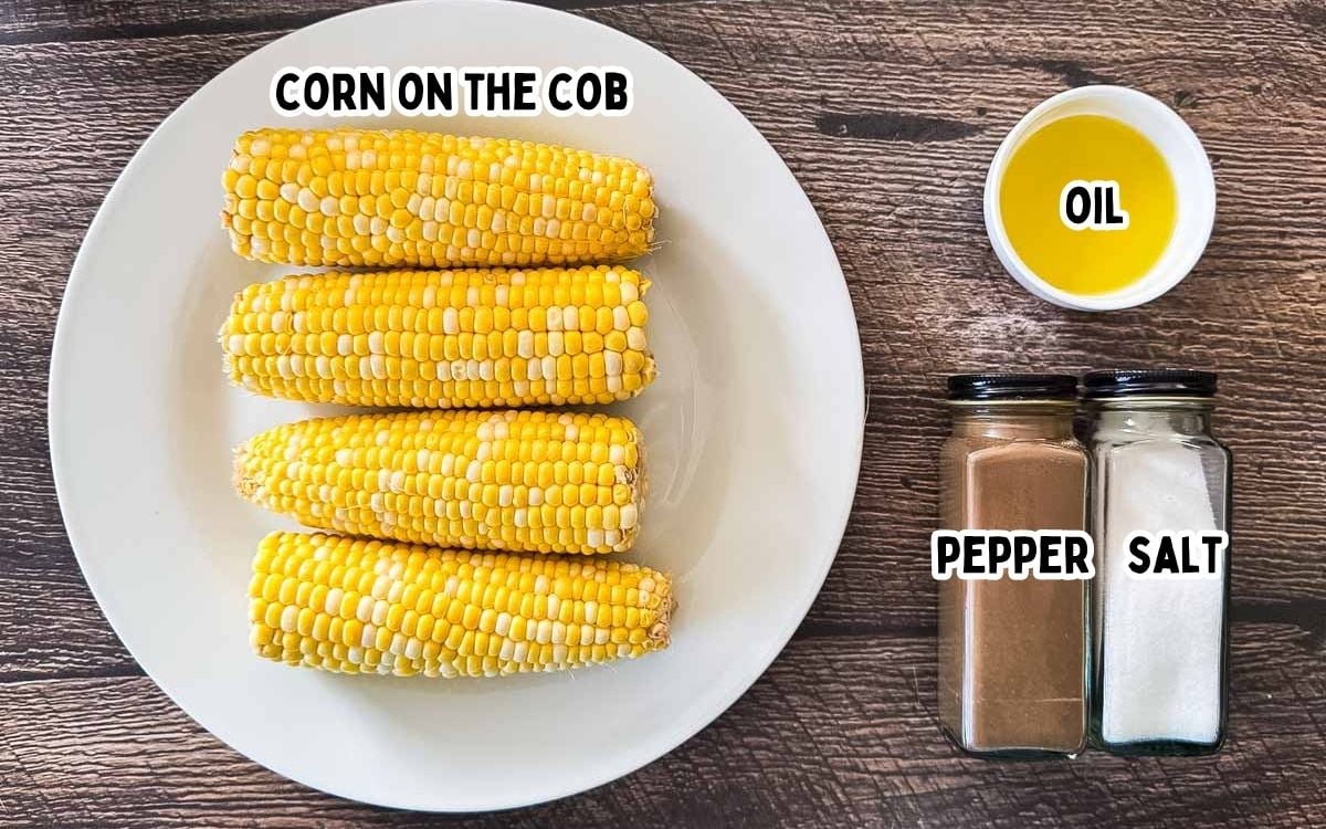 Ears of corn, butter, salt, black pepper, and parsley arranged on a countertop for air fryer corn on the cob.