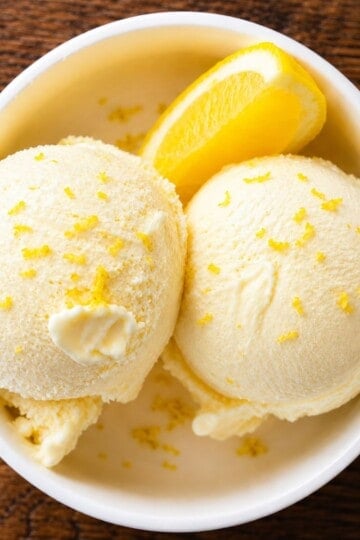 Ninja Creami lemon ice cream in a white bowl with lemon zest and fresh lemon slices.