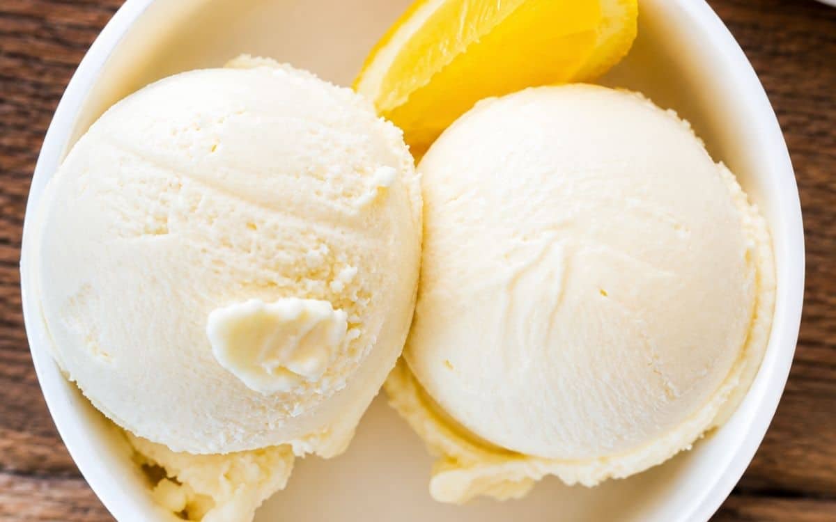 Two scoops of lemon ice cream in a white bowl with a lemon slice.