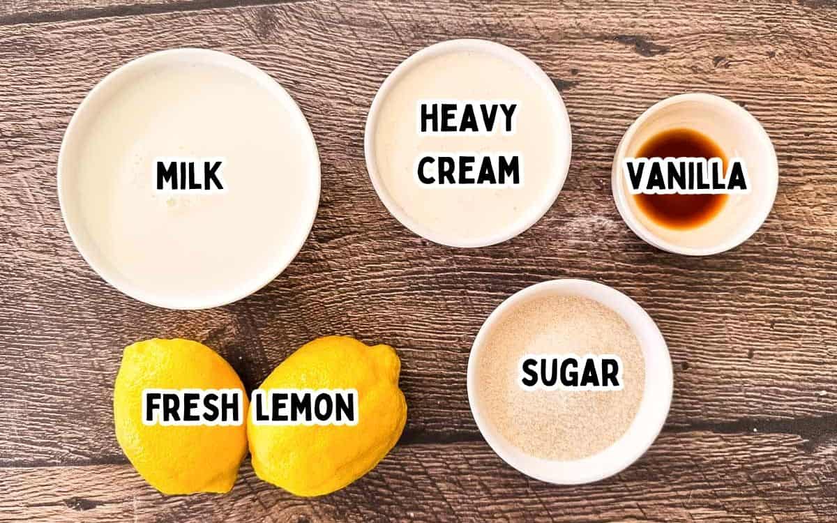 Ingredients for Ninja Creami lemon ice cream with bowls of milk, heavy cream, vanilla extract, sugar, and two fresh lemons on a wooden background.