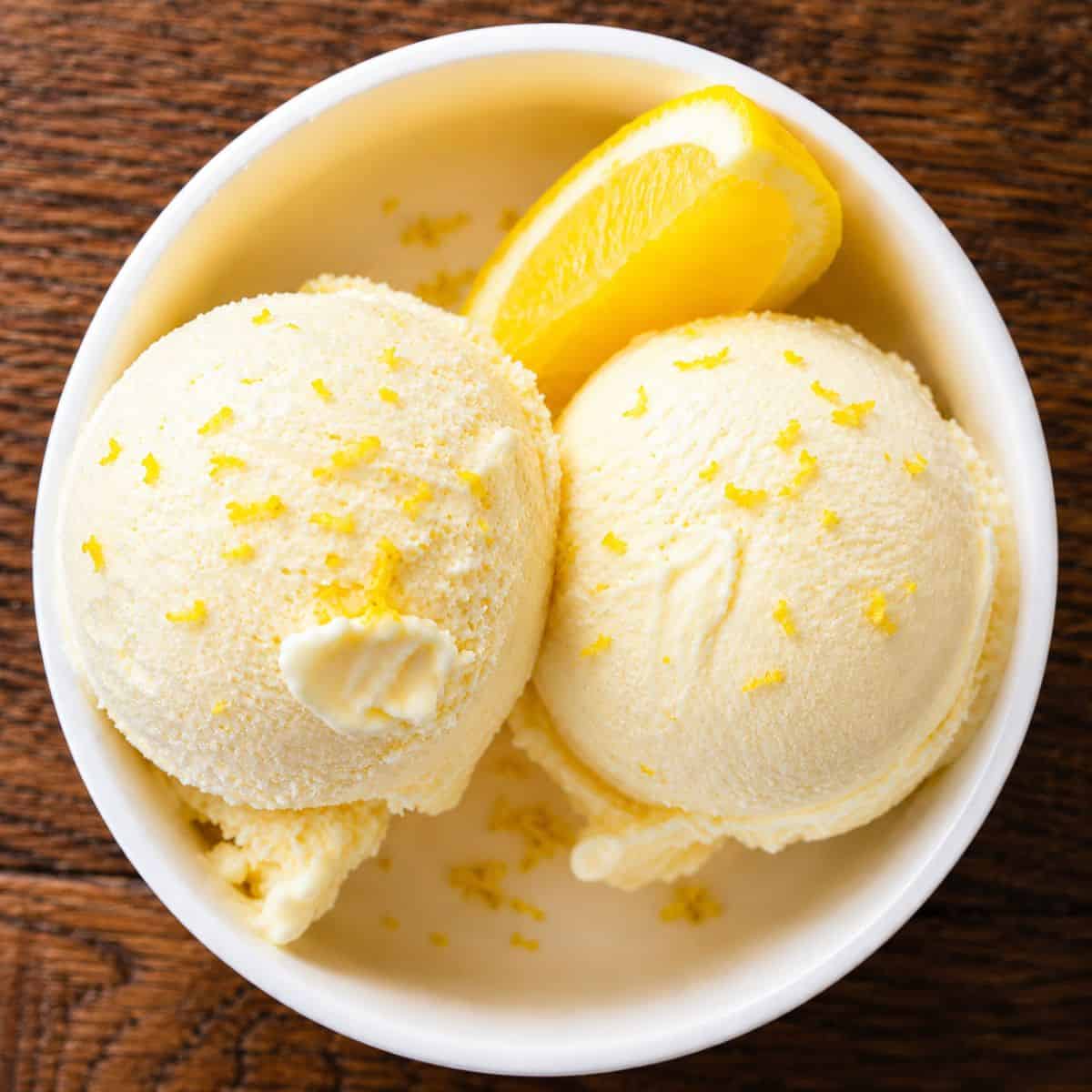 Ninja Creami lemon ice cream in a white bowl with lemon zest and fresh lemon slices.