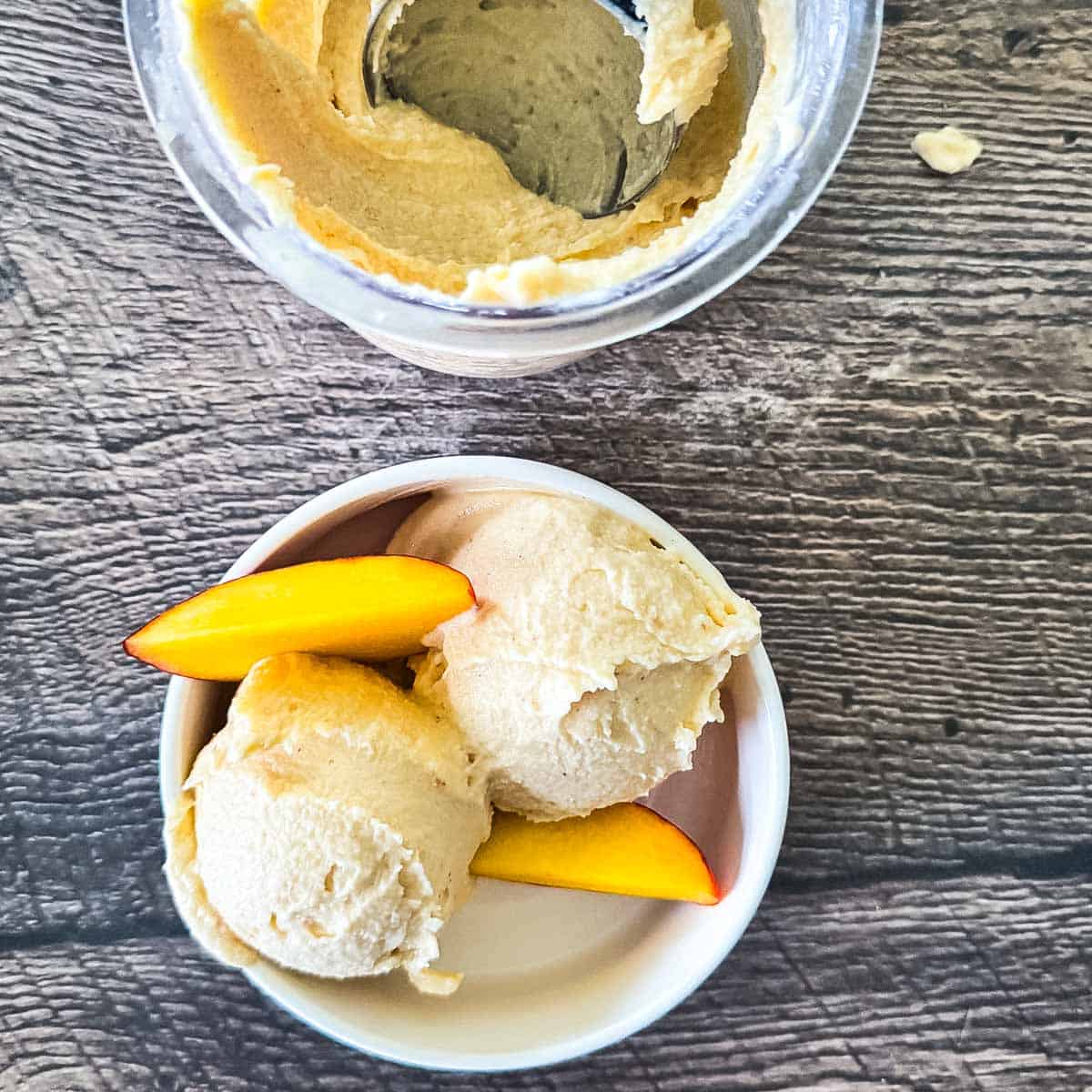 Two scoops of homemade peach ice cream in a white bowl with fresh peach slices.