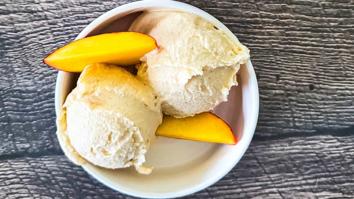 A scoop of homemade Ninja Creami peach ice cream in a chilled bowl, topped with fresh peach slices.