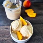 Two scoops of creamy Ninja Creami peach ice cream in a white bowl, topped with fresh peach slices.