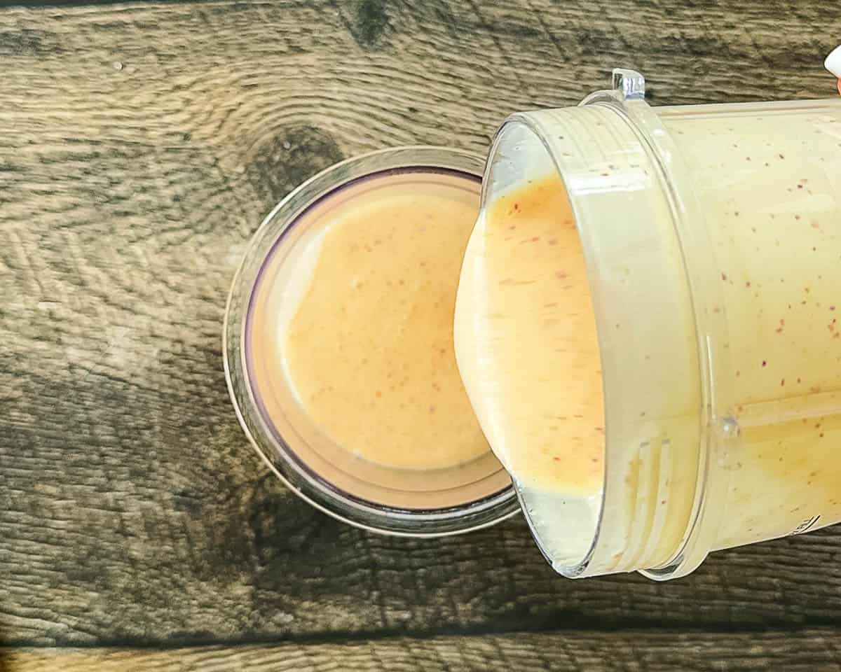 Peach ice cream base being poured into a Ninja Creami pint container up to the max fill line.