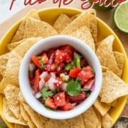 A crisp white bowl filled with fresh keto pico de gallo, nested perfectly in the center of a large yellow bowl overflowing with tortilla chips.