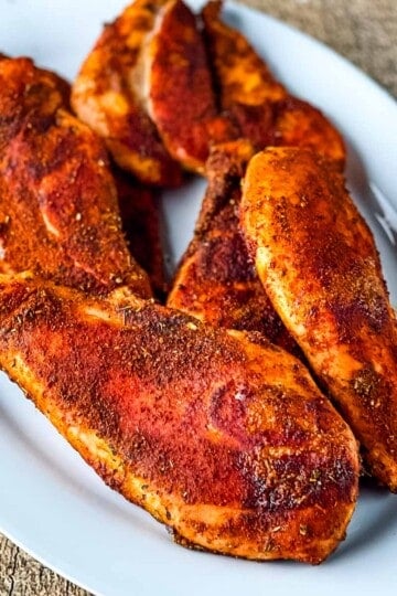 Smoked chicken breasts with Cajun seasoning on a white plate.