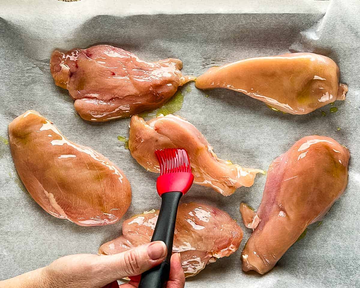 Brushing olive oil onto raw chicken breasts before smoking.