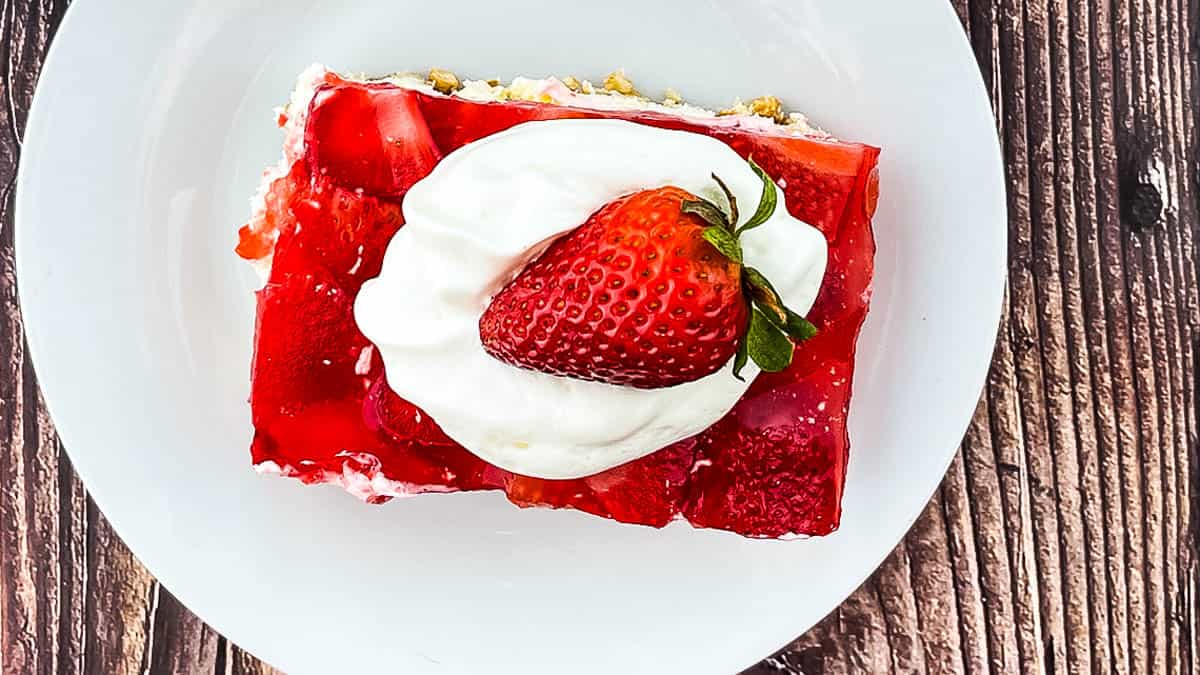 Overhead view of strawberry pretzel salad square topped with whipped cream and fresh strawberry.