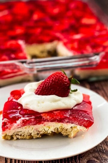 Slice of strawberry pretzel salad topped with whipped cream and a fresh strawberry on a white plate.