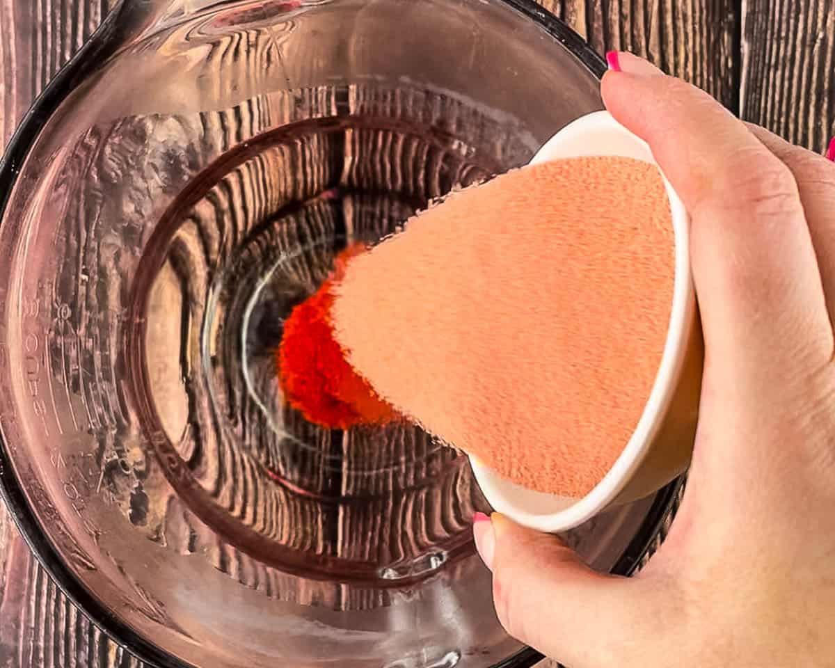 Pouring strawberry Jell-O powder into a glass mixing bowl.
