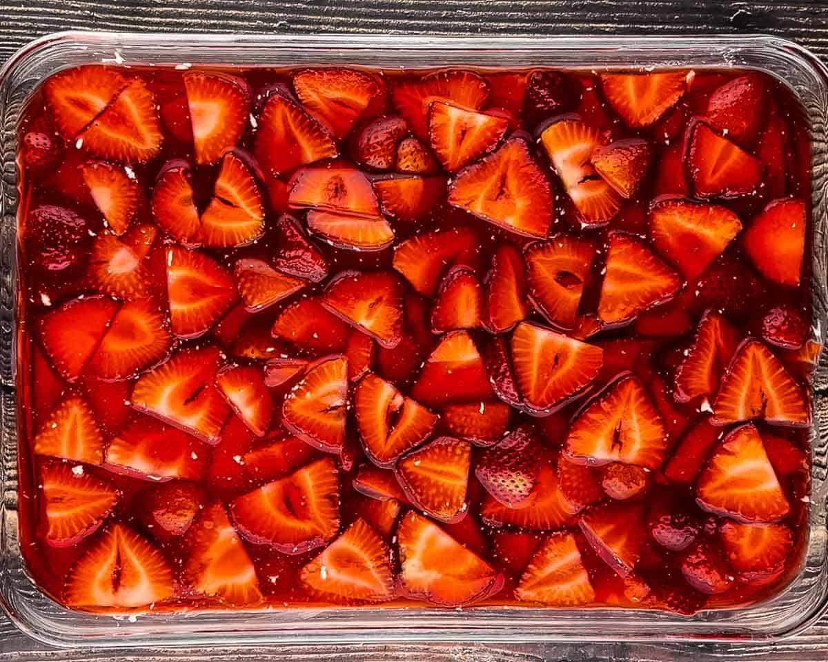Strawberry Jell-O and fresh strawberry topping spread over cream cheese layer in baking dish.