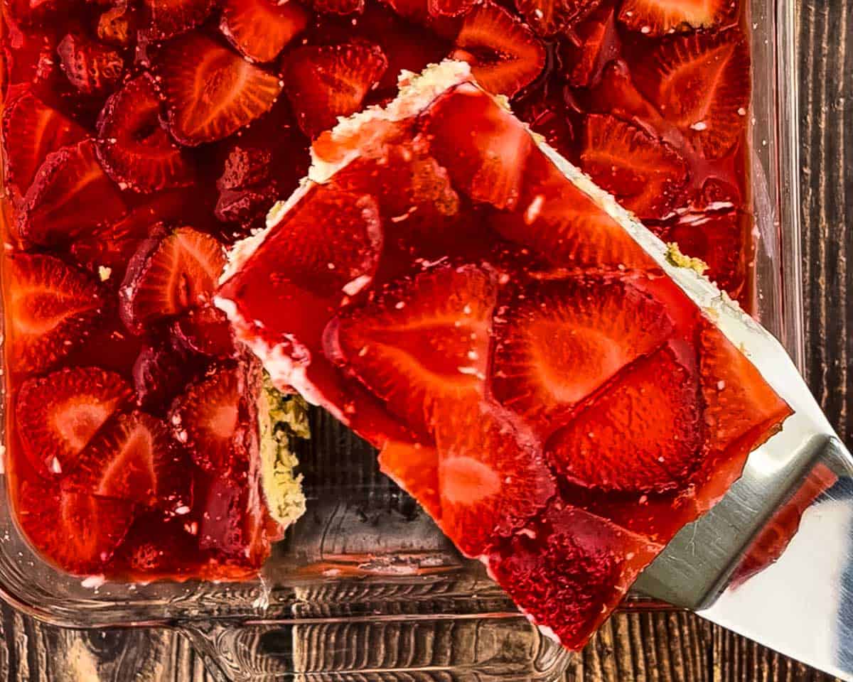 Lifting a square of strawberry pretzel salad from a glass baking dish with a spatula.