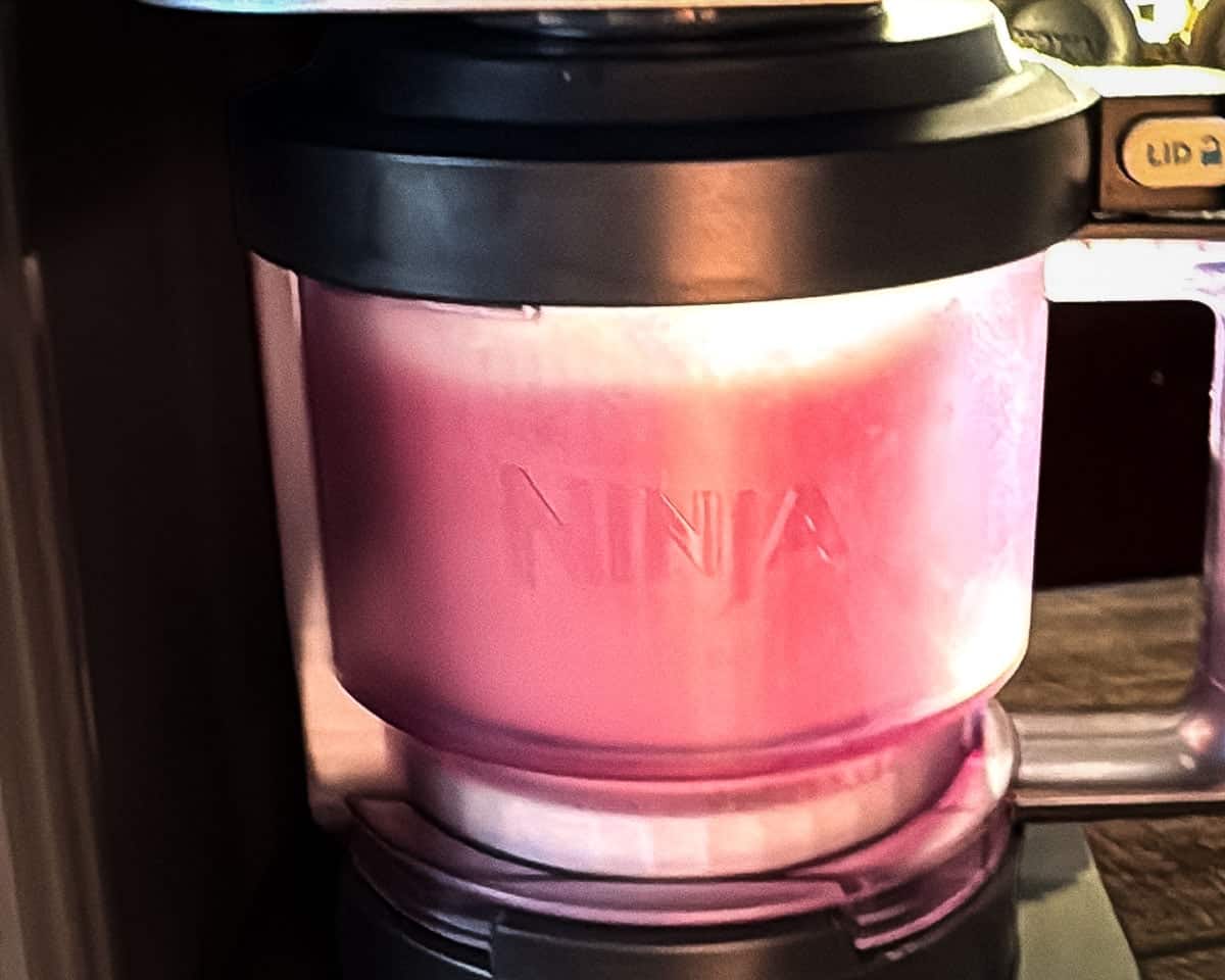 The Ninja Creami machine processing the mixture on the LITE ICE CREAM setting.