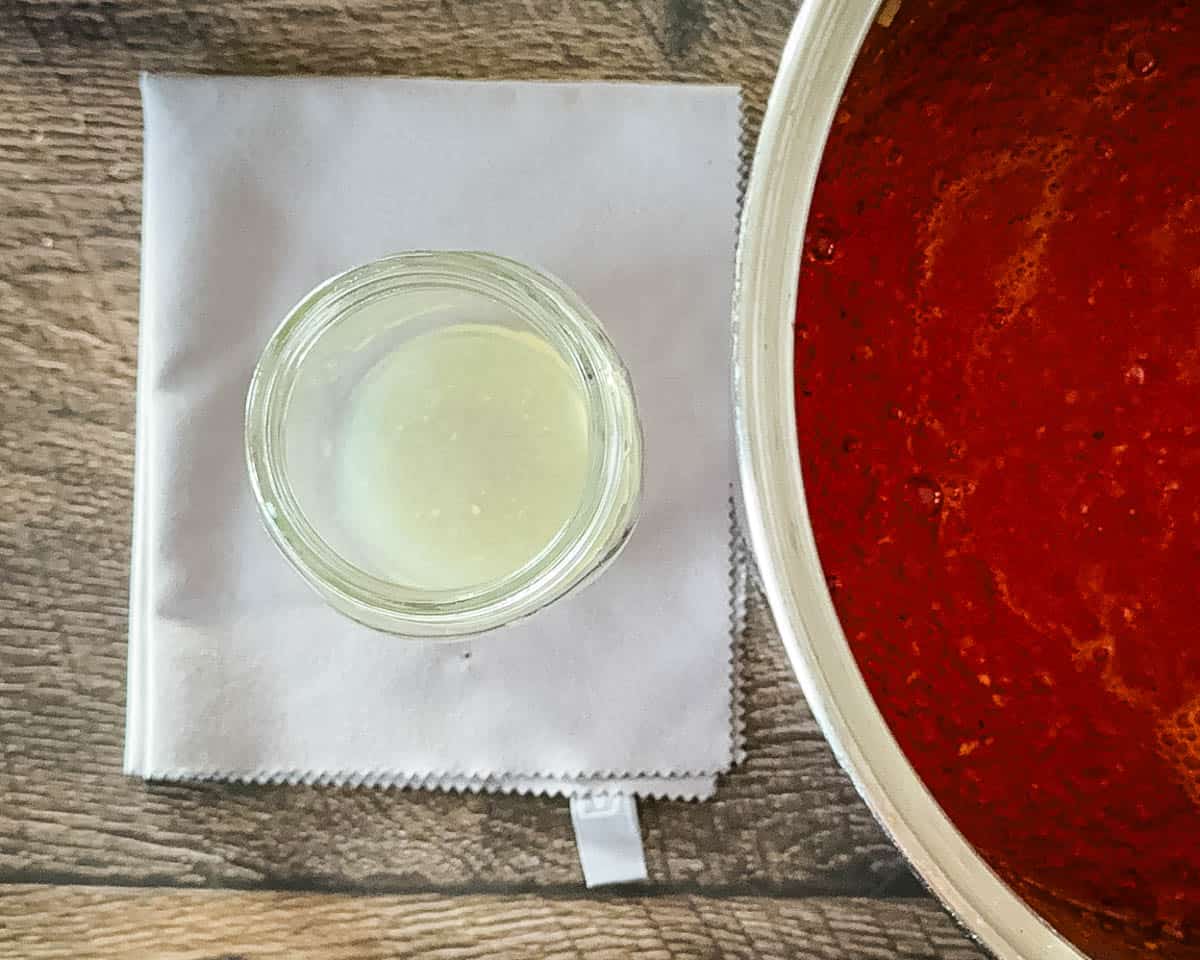 Adding bottled lemon juice to clean canning jars before filling with tomato sauce.