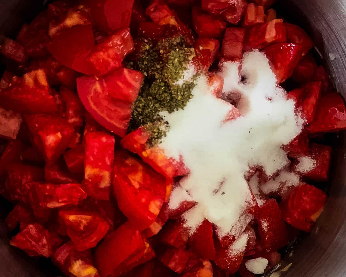 Fresh tomatoes simmering in a large pot with herbs and sugar.