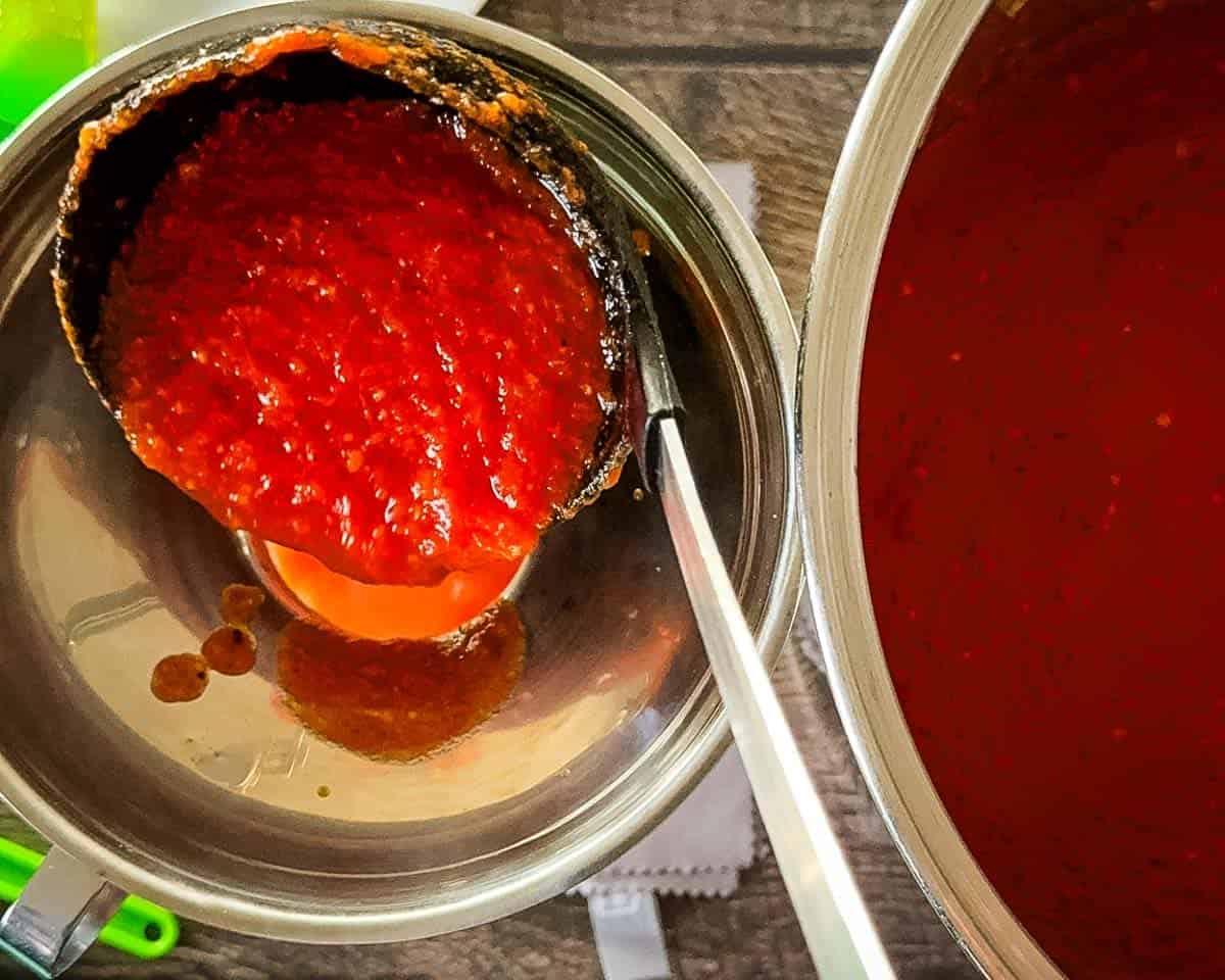 Ladling hot homemade tomato sauce into mason jars for canning.
