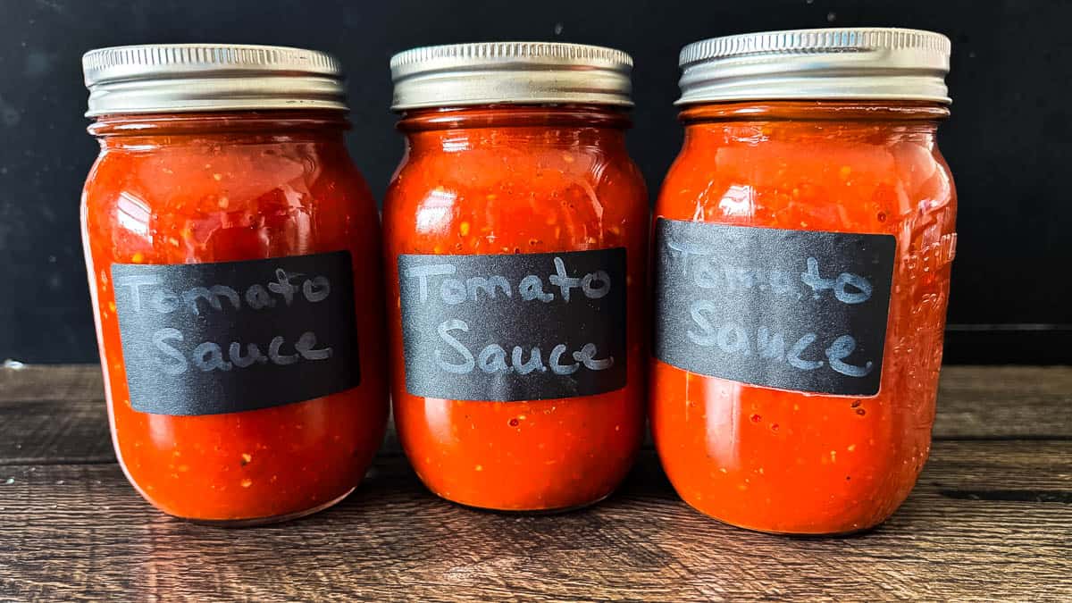 Three mason jars filled with homemade canned tomato sauce on a wooden countertop.