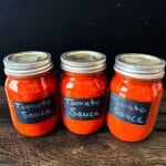Three jars of homemade canned tomato sauce made with fresh tomatoes using water bath canning.